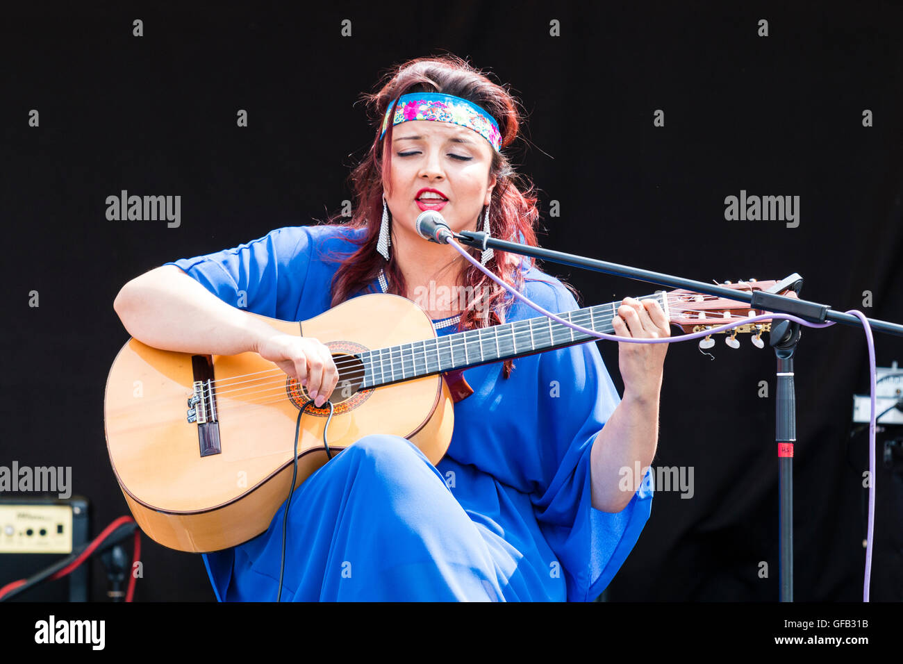 Columbian songwriter, singer and guitarist, Carolina Herrera in blue dress, playing guitar and singing while sitting on an open air stage at Ramsgate. Stock Photo