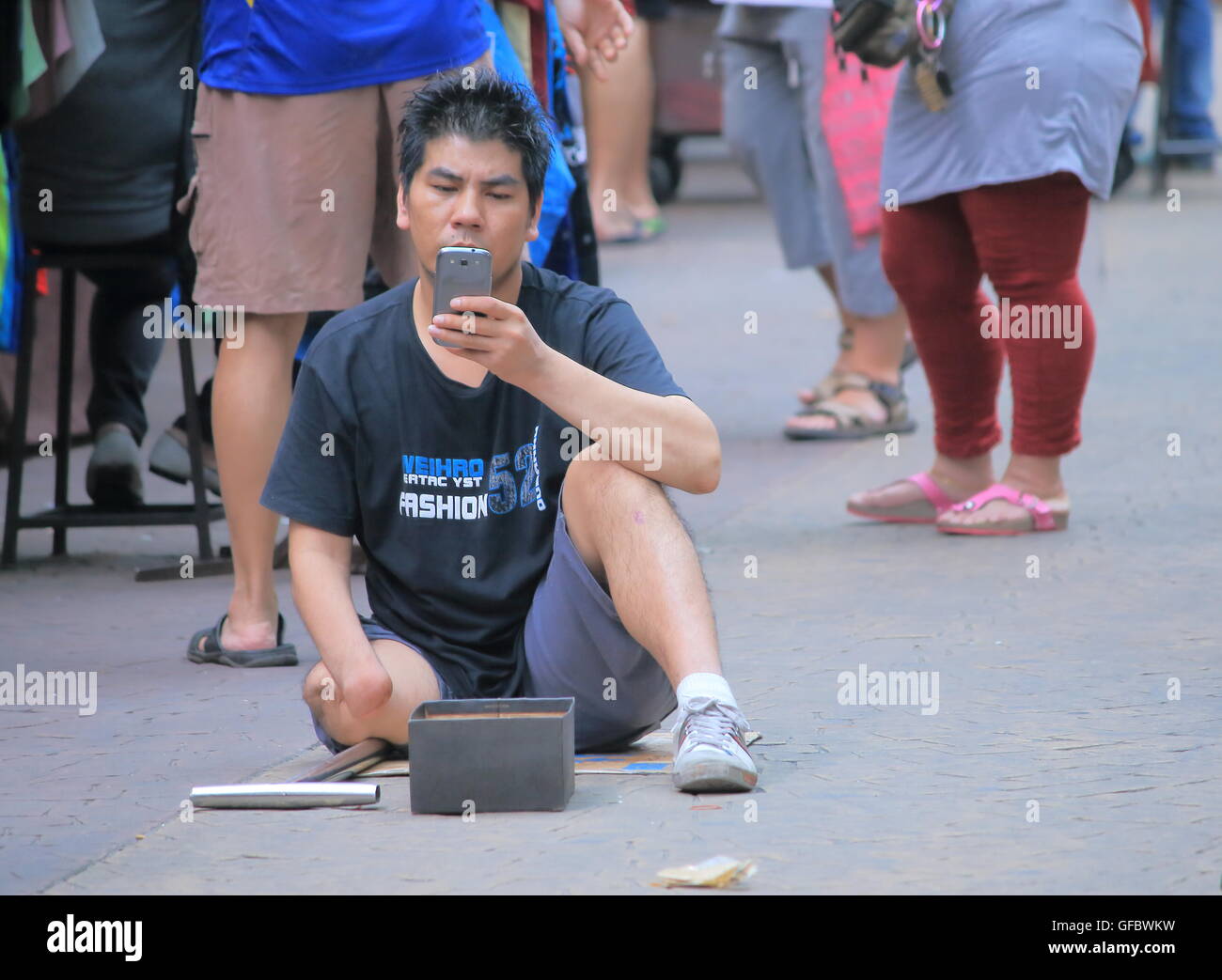 A disable man begs at China town while playing with a phone in Kuala Lumpur Malaysia. Stock Photo