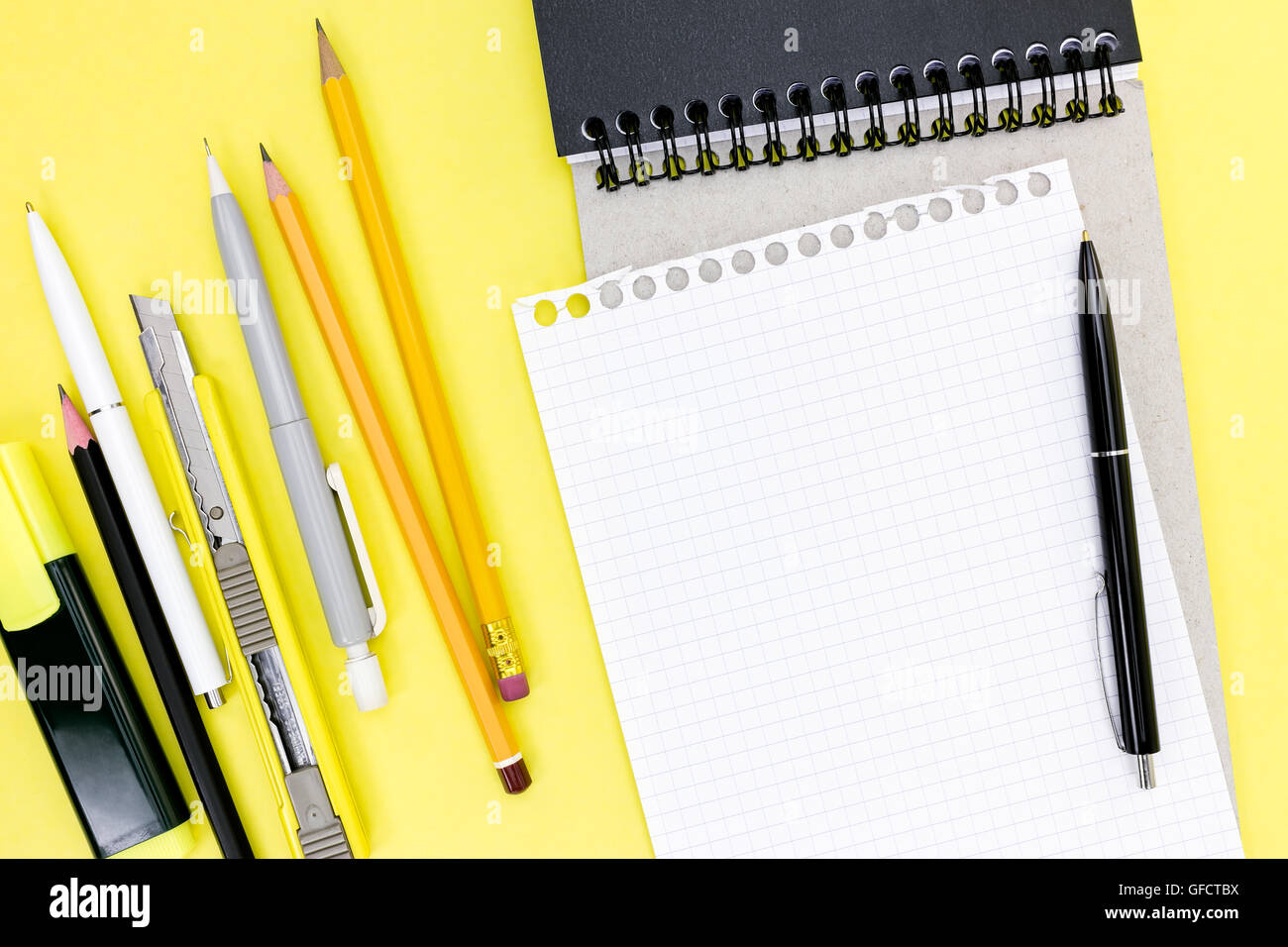 office supplies, notebook and squared piece of paper on yellow writing desk background Stock Photo