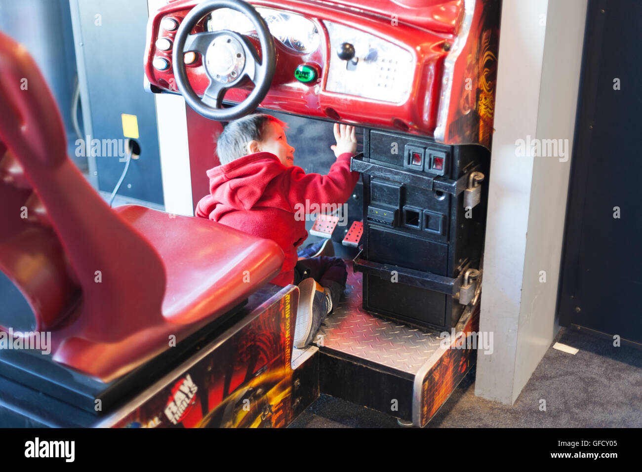 Rear view of a boy playing driving game at video game arcadecolor image ...