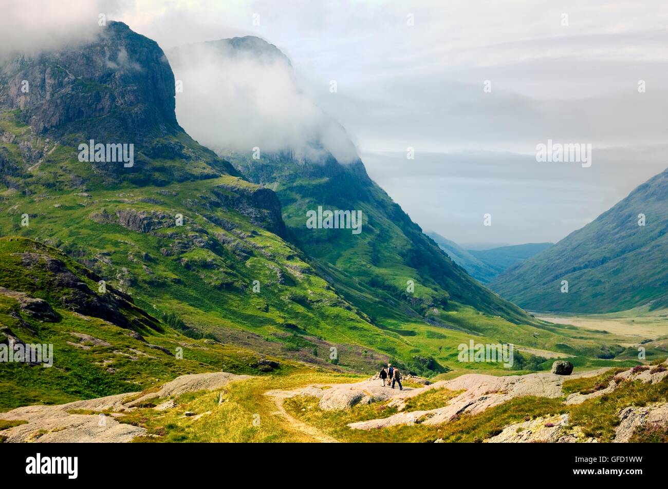 Walkers on path in the Pass of Glencoe with the craggy back drop of the Three Sisters. Highland Region, Scotland Stock Photo