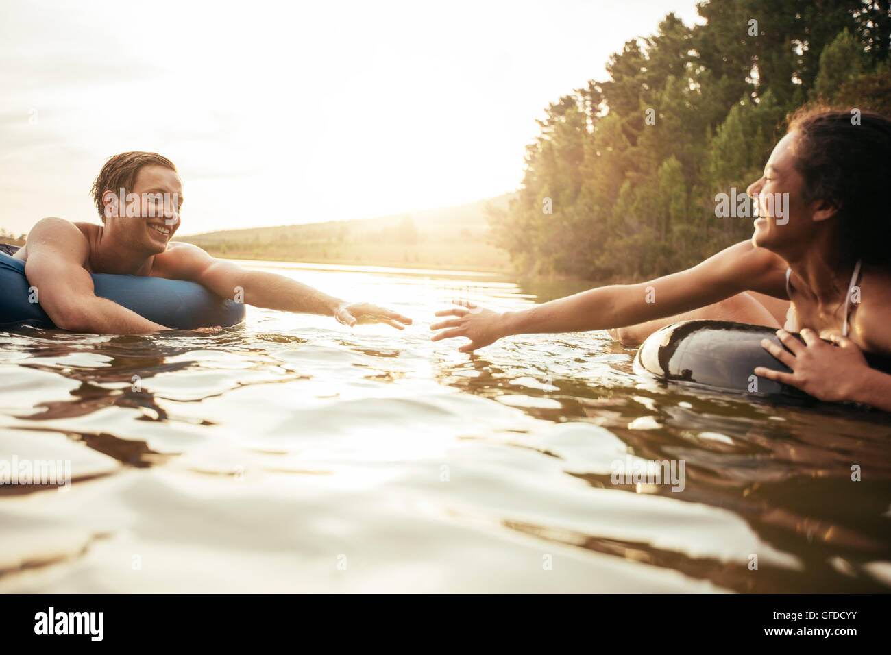 Affectionate young couple about to hold hands while floating on inner tubes in water. Young man and woman in an inflatable tube Stock Photo