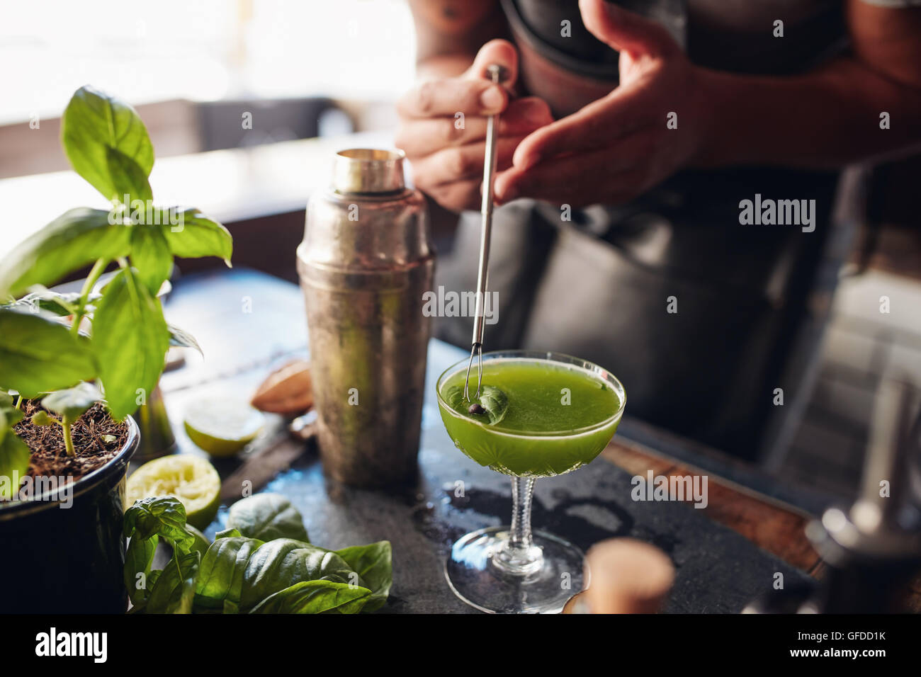 Close up shot of barman hands garnishing fresh basil smash cocktail at the counter Stock Photo
