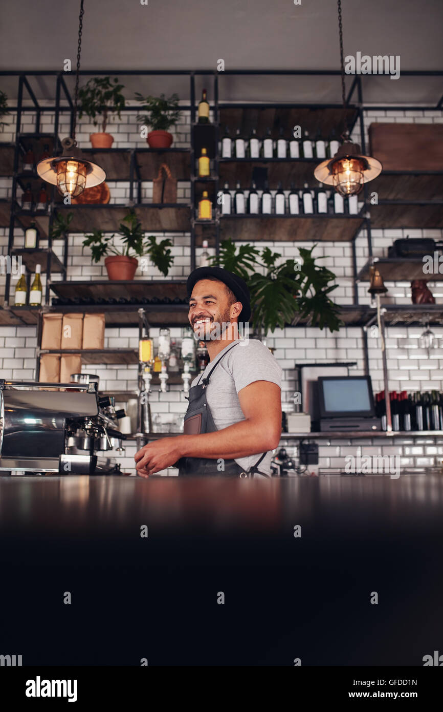 Portrait of a young business owner standing in a cafe. Handsome young man wearing apron standing by bar counter looking away and Stock Photo