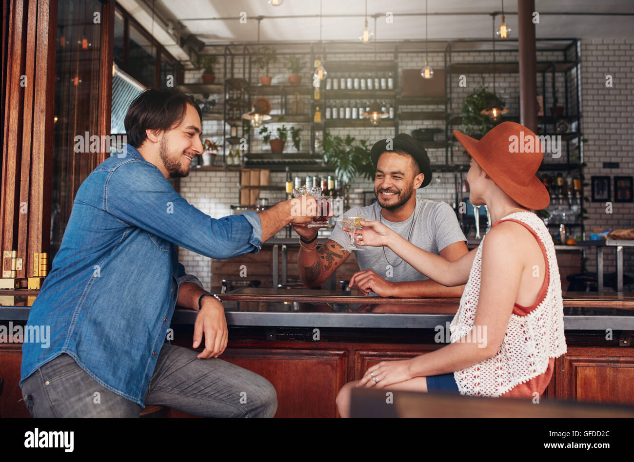 Three young people sitting in the restaurant and having a toast. Group of friends at a cafe having a drink and toasting. Stock Photo