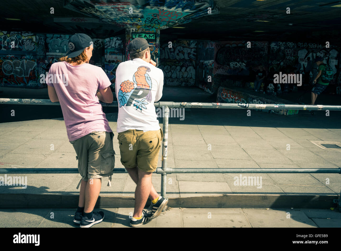 Two young men watch skateboarders doing tricks under the Royal Festival Hall in the Southbank Centre, London, UK Stock Photo