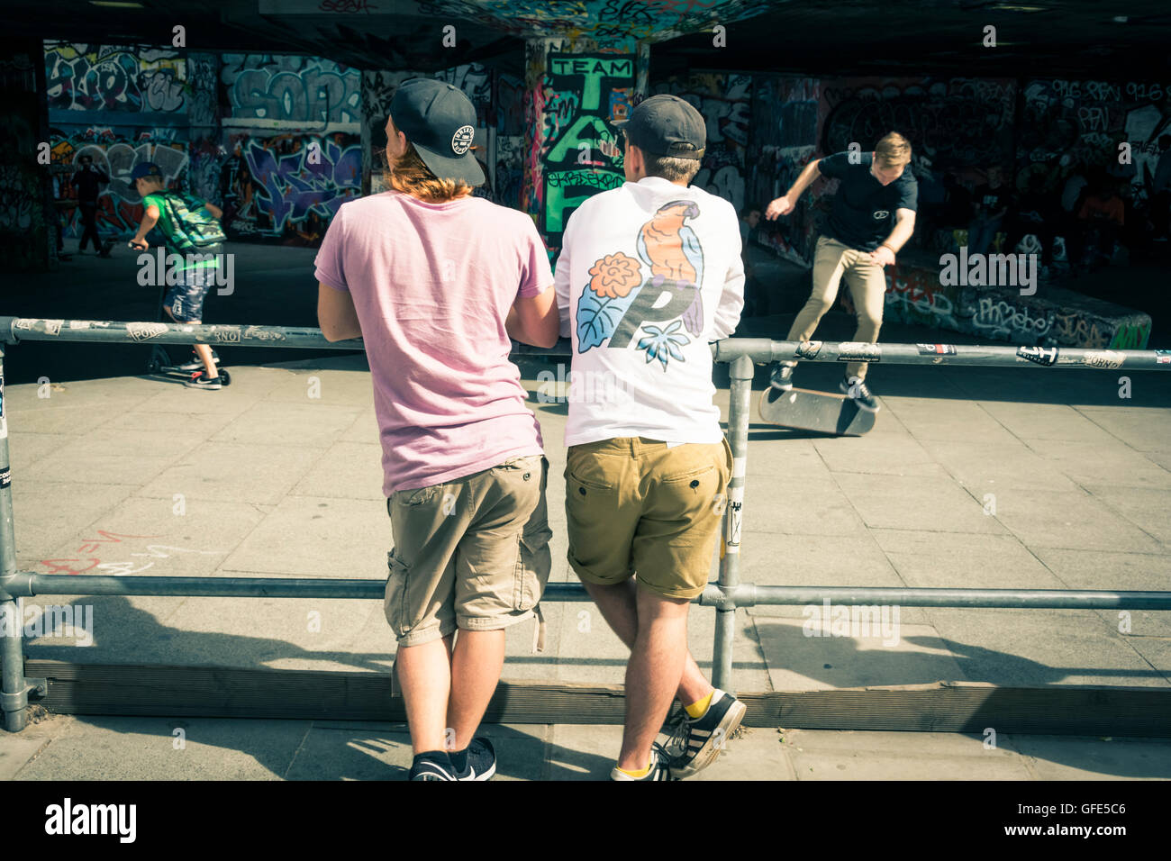 Two young men watch skateboarders doing tricks under the Royal Festival Hall in the Southbank Centre, London, UK Stock Photo