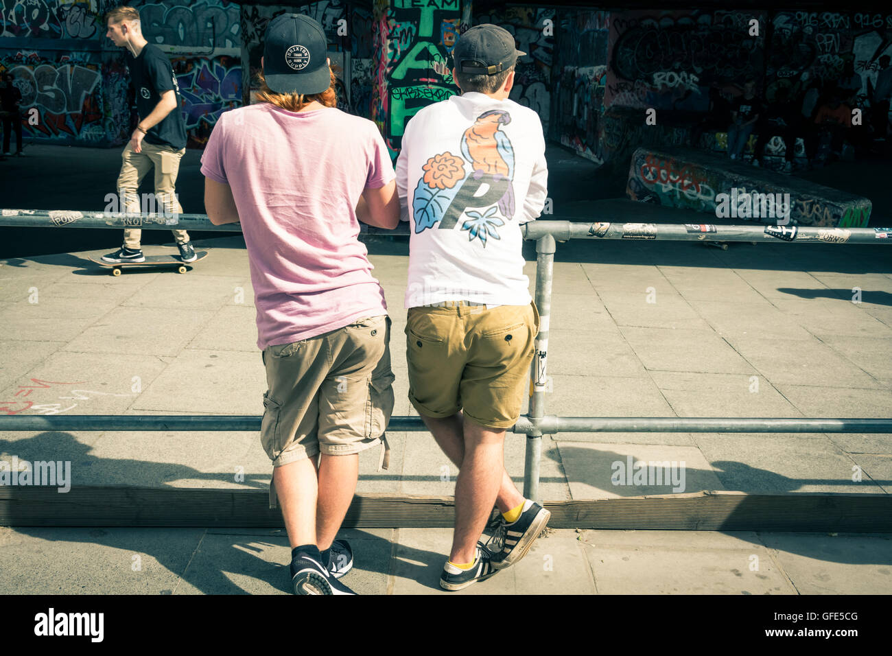 Two young men watch skateboarders doing tricks under the Royal Festival Hall in the Southbank Centre, London, UK Stock Photo