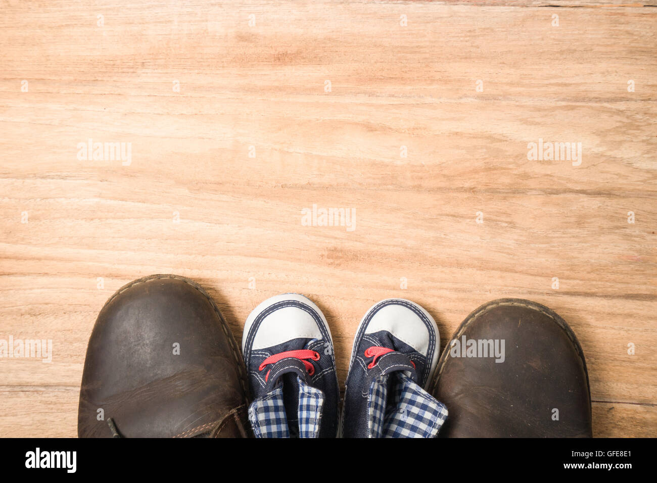 Daddy's boots and baby's sneakers, on wood background, fathers day concept. Stock Photo