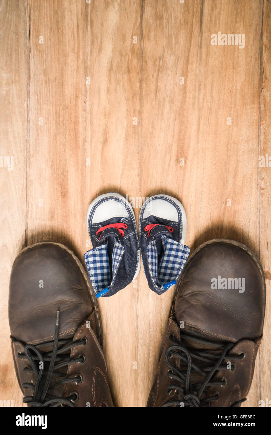Daddy's boots and baby's sneakers, on wood background, fathers day concept. Stock Photo