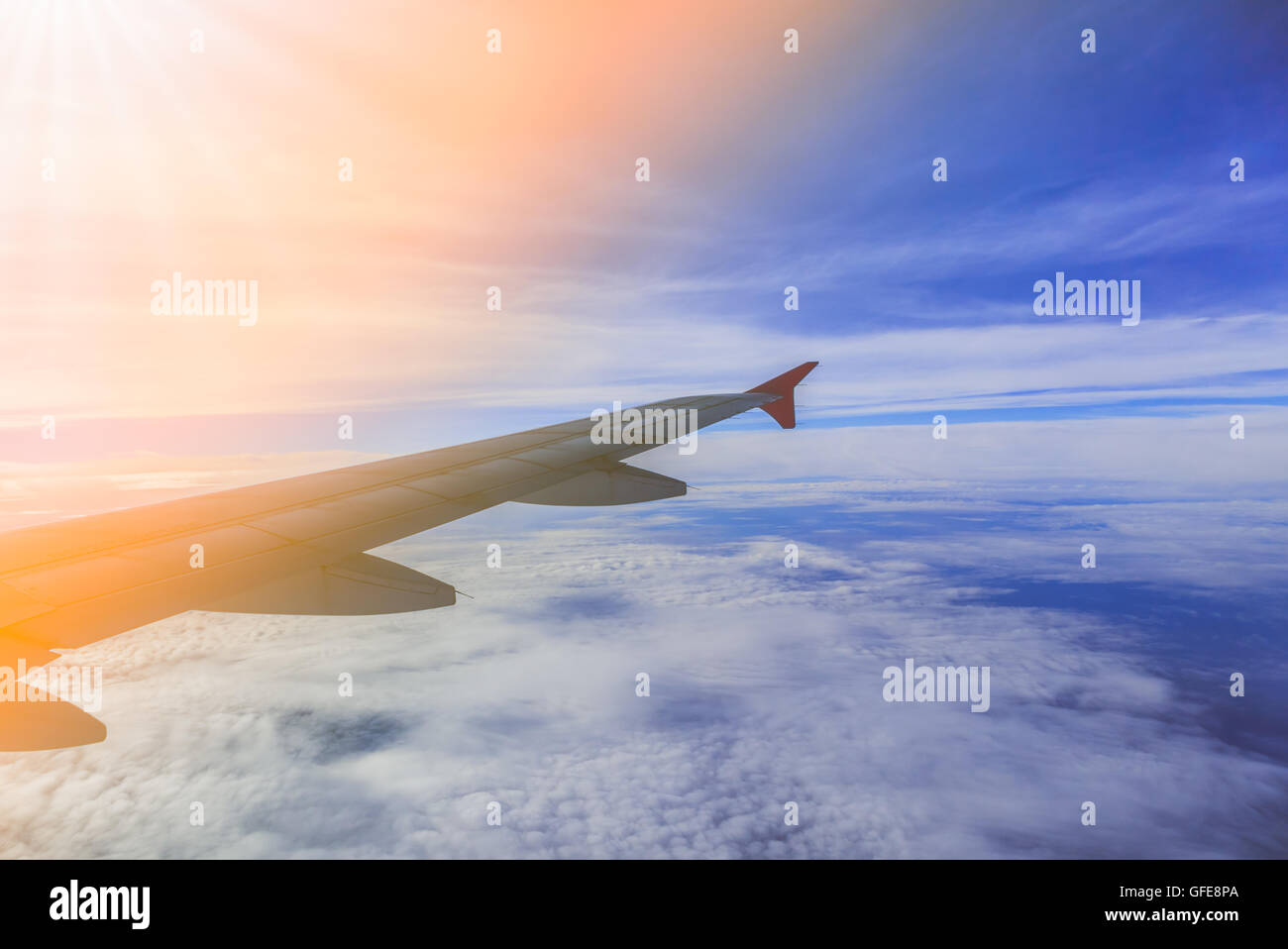 Airplane flying above clouds at sunrise filter Stock Photo