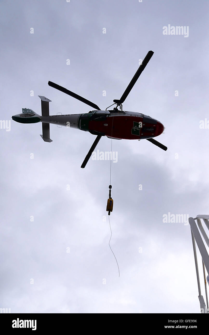 Helicopter flies over container ship Utrillo with cable and belt ready secured to collect pilot from deck. Stock Photo