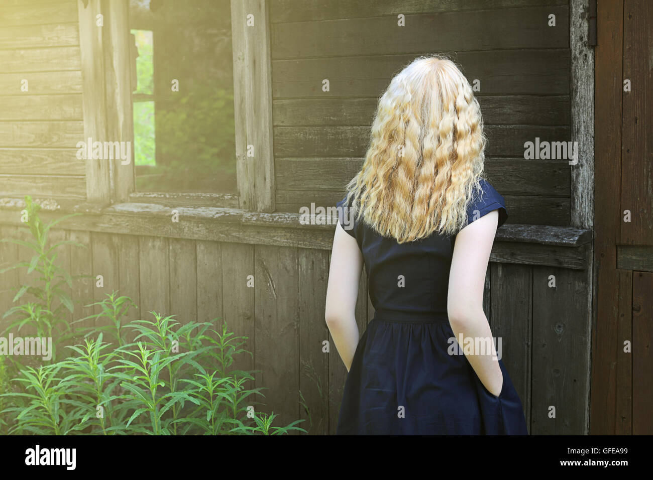 Girl with long blond hair standing at the old shed Stock Photo