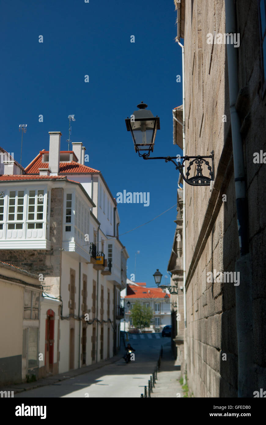 Detail of street in Betanzos against a deep blue sky. A motorbike comes from the distance. Stock Photo