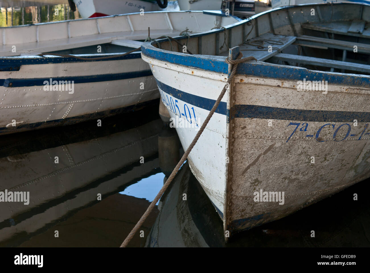 close up of boats on still water on sunny day. The water mirrors the boats above it. Stock Photo