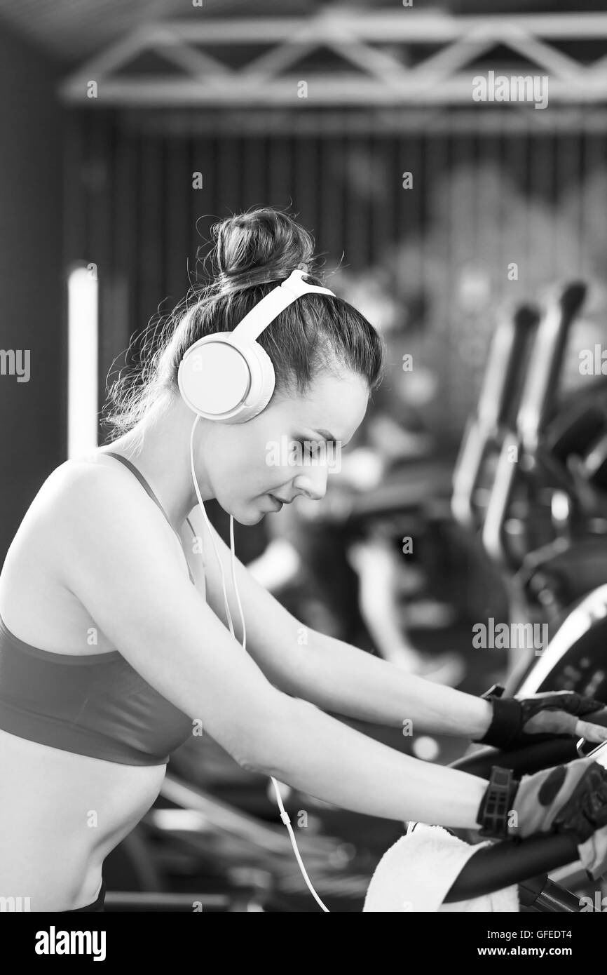 Young woman with headphones doing exercises on stationery bicycle in a gym or fitness center Stock Photo