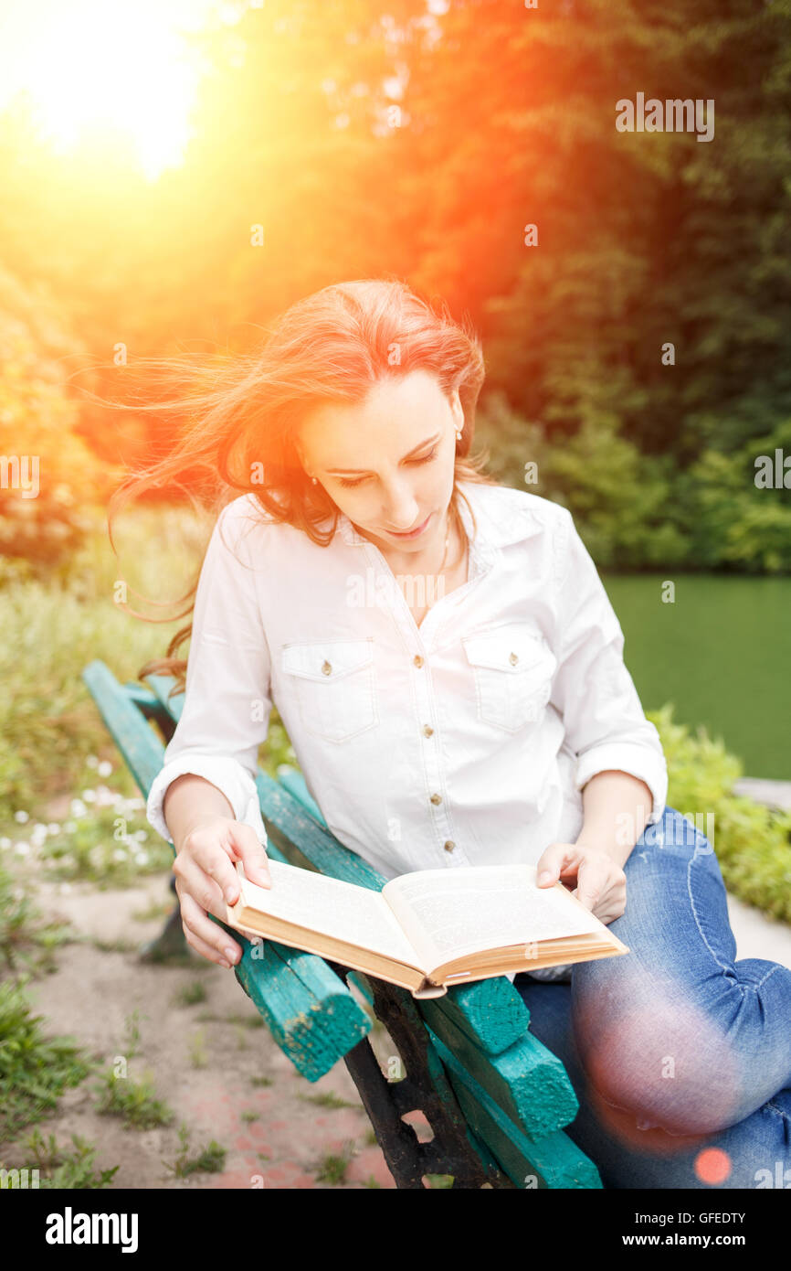 Young woman sitting on the bench in a park and reading a book ...