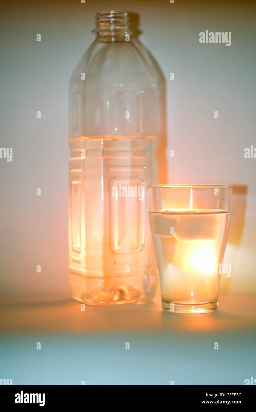 a back lit glass and bottle of refreshing mineral water with ice cubes ...