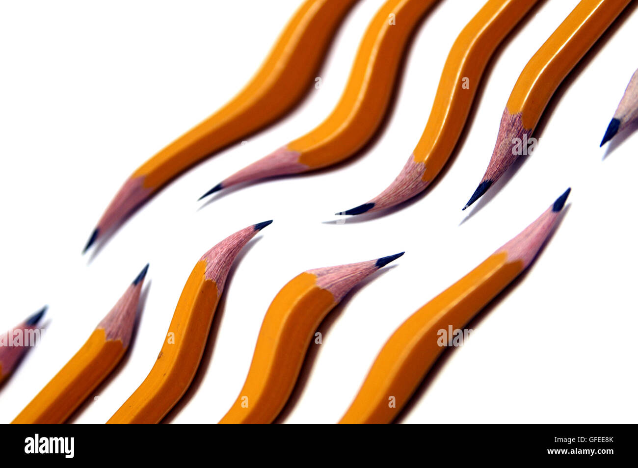 10 sharp distorted yellow wooden pencils, wave shaped, on white background Stock Photo