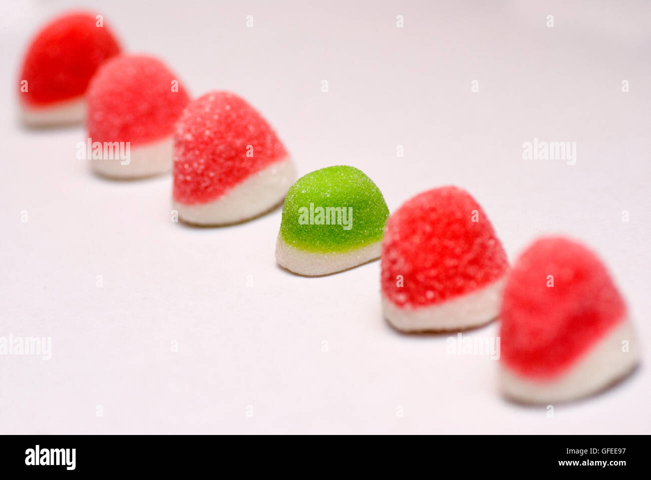 A line of red colourful sugared jelly sweets with one green one in the
