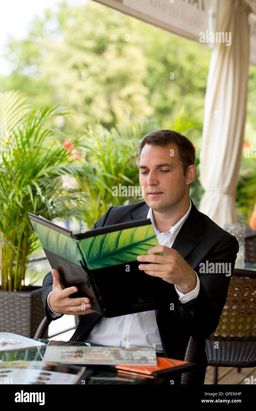 Young Businessman holding a menu sitting in a summer restaurant Stock Photo