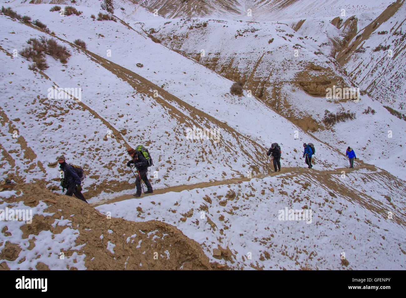 Trekkers walking along a treacherous trail at the edge of snow covered mountain in Ladakh (India) during winter Stock Photo
