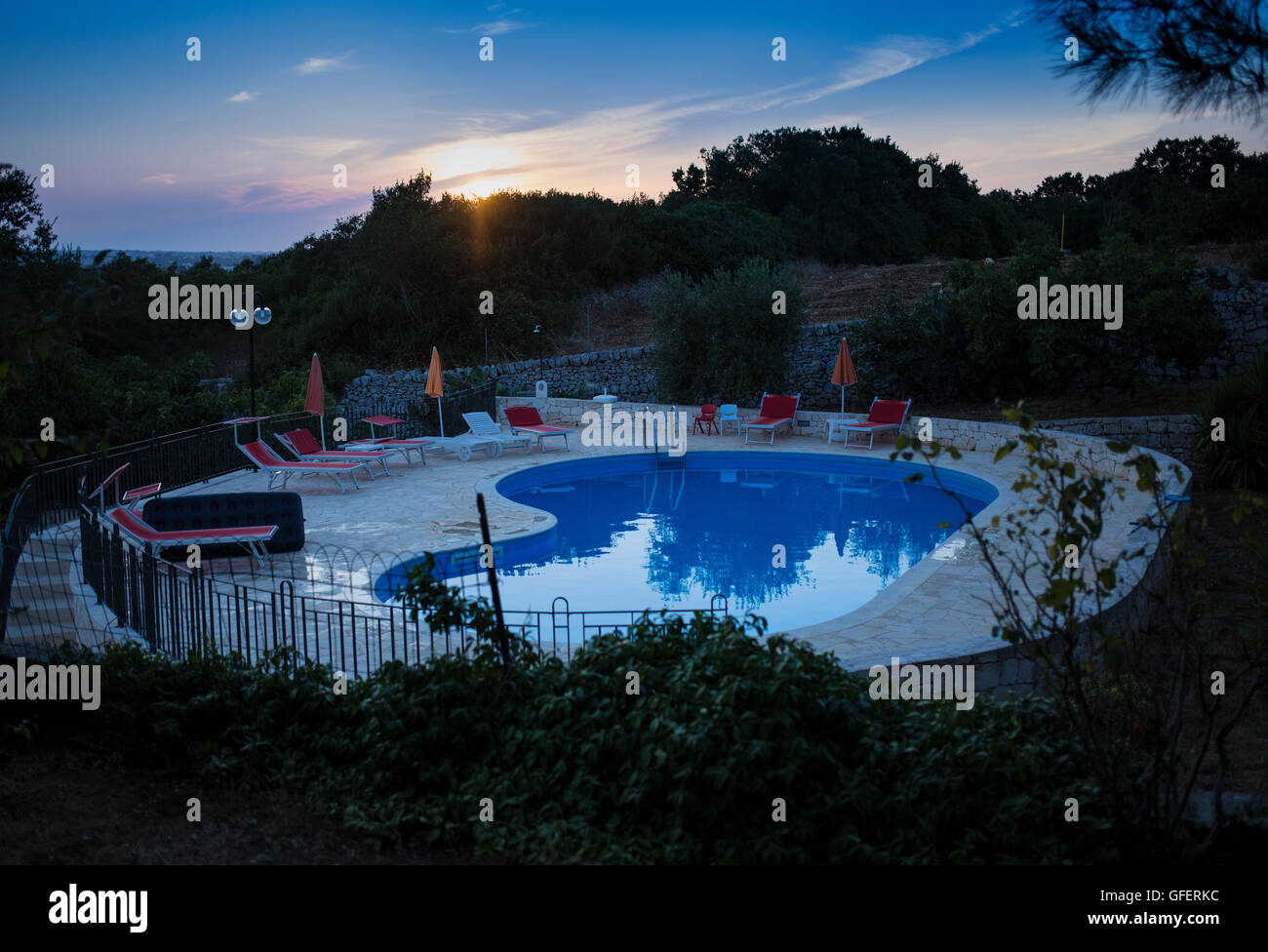 The sun sets over a swimming pool at Trulli Beltramonto holiday apartments in Locorotondo, Puglia, Italy Stock Photo