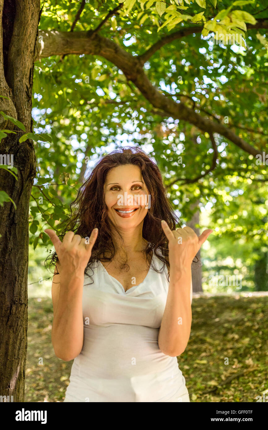 Close Up Of Busty Classy Mature Woman Smiling At The Camera While Doing Welcome Shaka Sign Against Green Garden Background With Copy Space Stock Photo Alamy