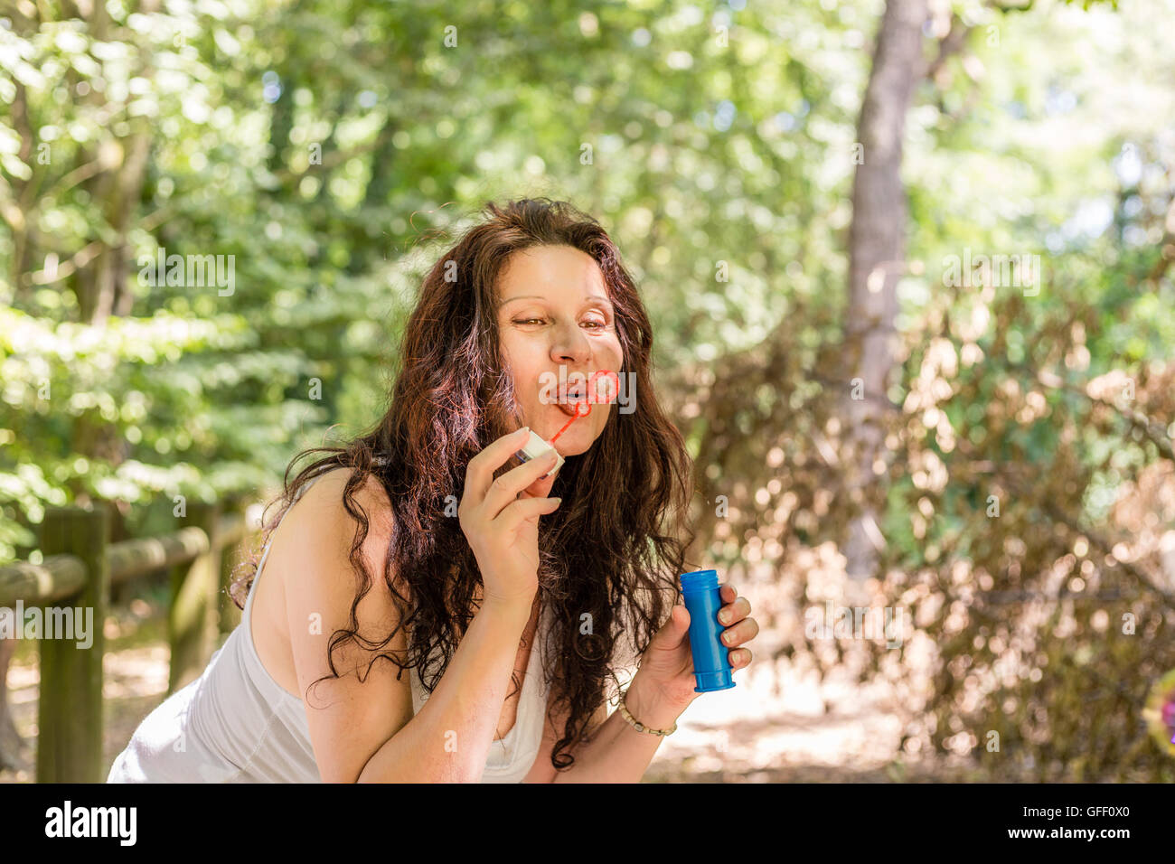 Fascinating mature adult woman is having fun like a little girl blowing soap bubbles in a public park Stock Photo