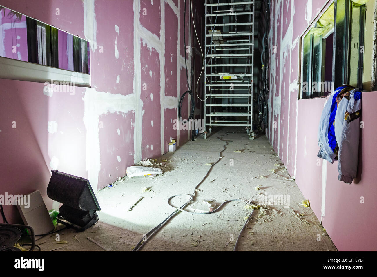 Searchlight is sheds light on mobile scaffold placed in long corridor made of plasterboard. Stock Photo