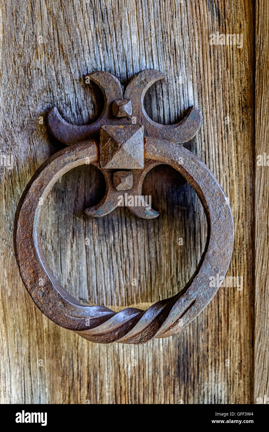 Ornate ancient rusty iron door knocker on section of wooden door Stock Photo
