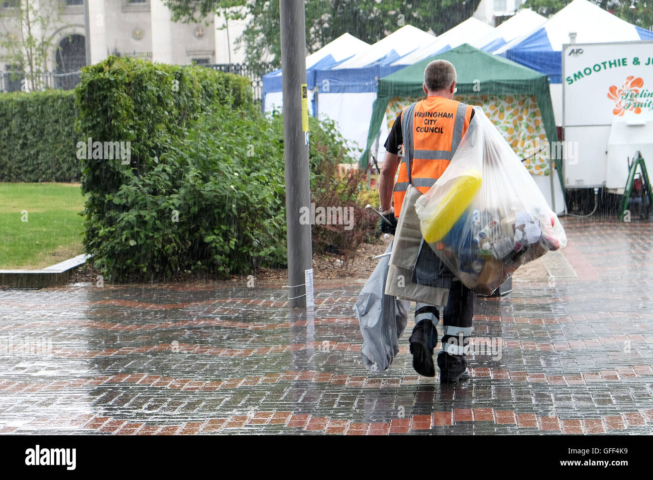 A council worker clears away bags of rubbish during a sudden summer rain storm in a busy city centre area Stock Photo