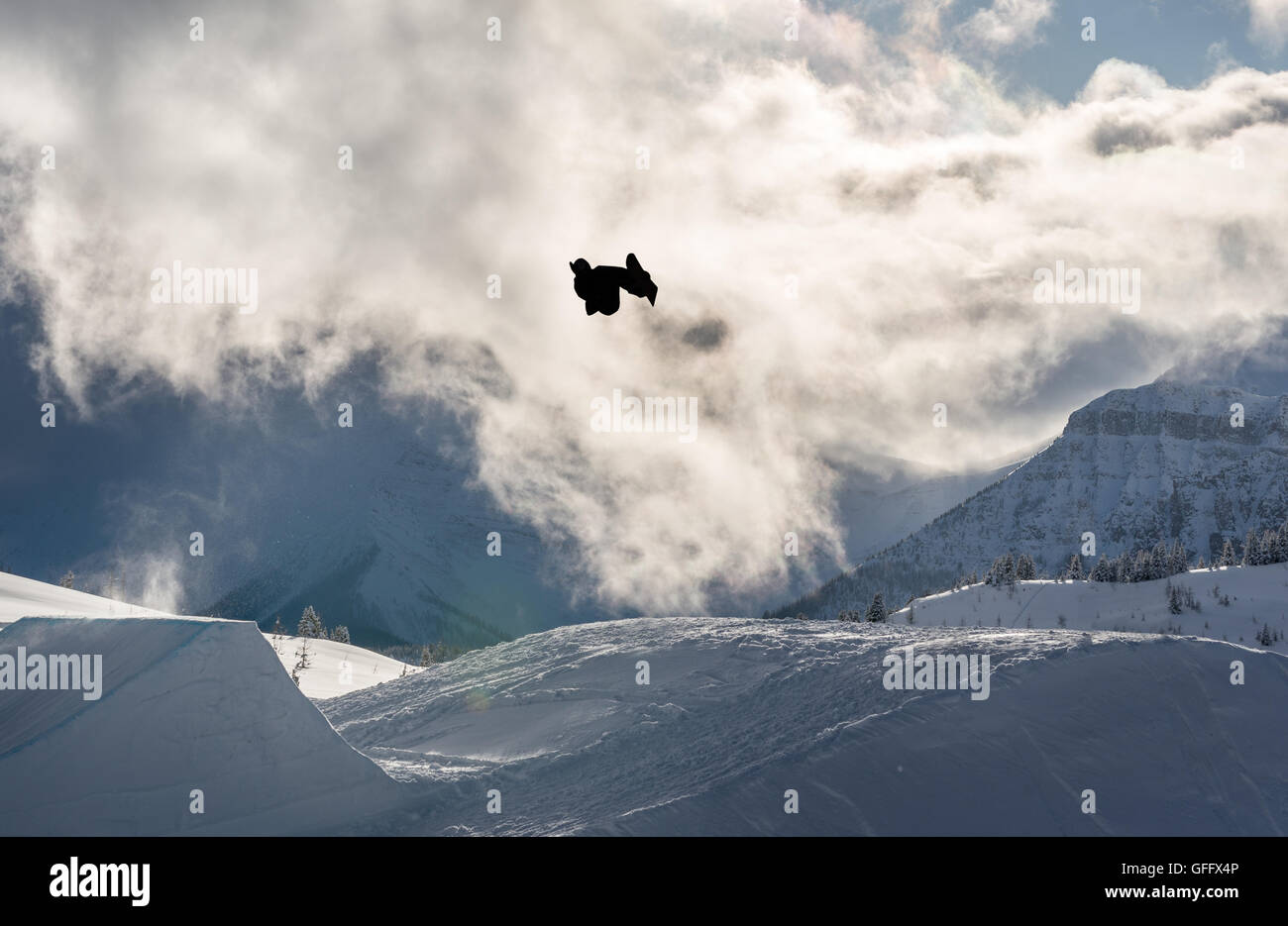Snowboarder performing a flip off a large jump in the mountains Stock Photo