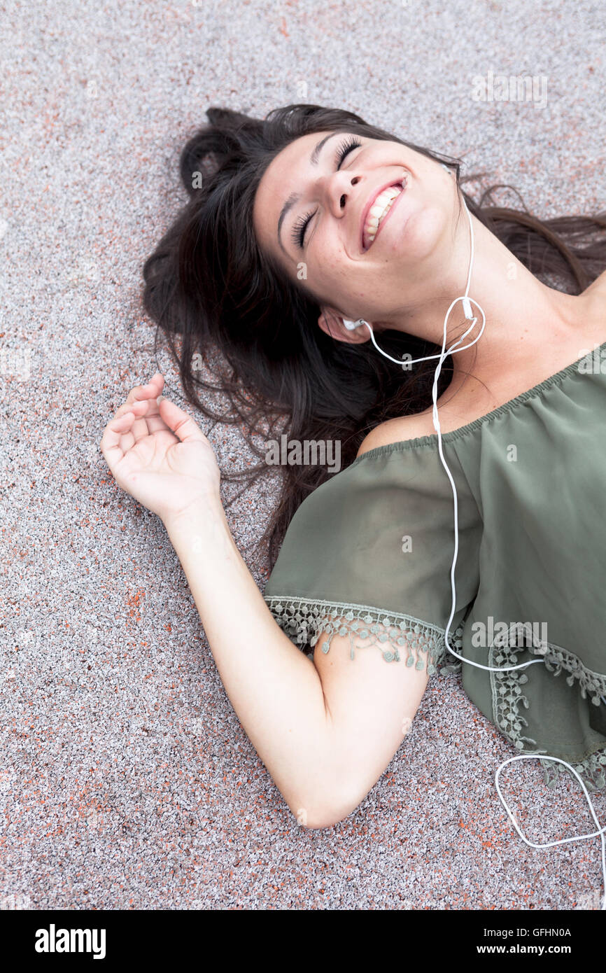 Portrait of young girl listening to music lying on the floor of urban ...
