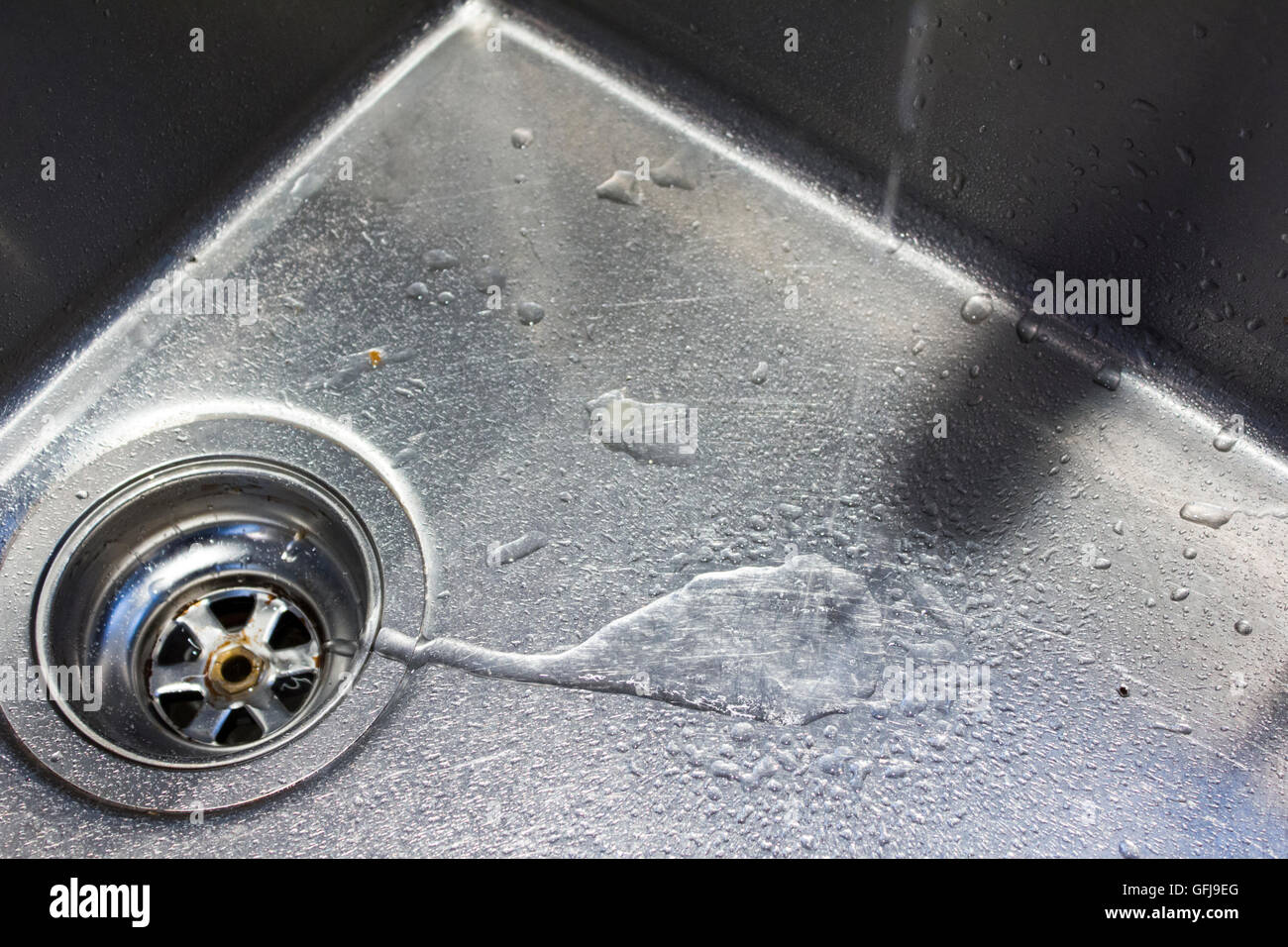 Water from a tap runs down the drain in a stainless steel sink Stock Photo