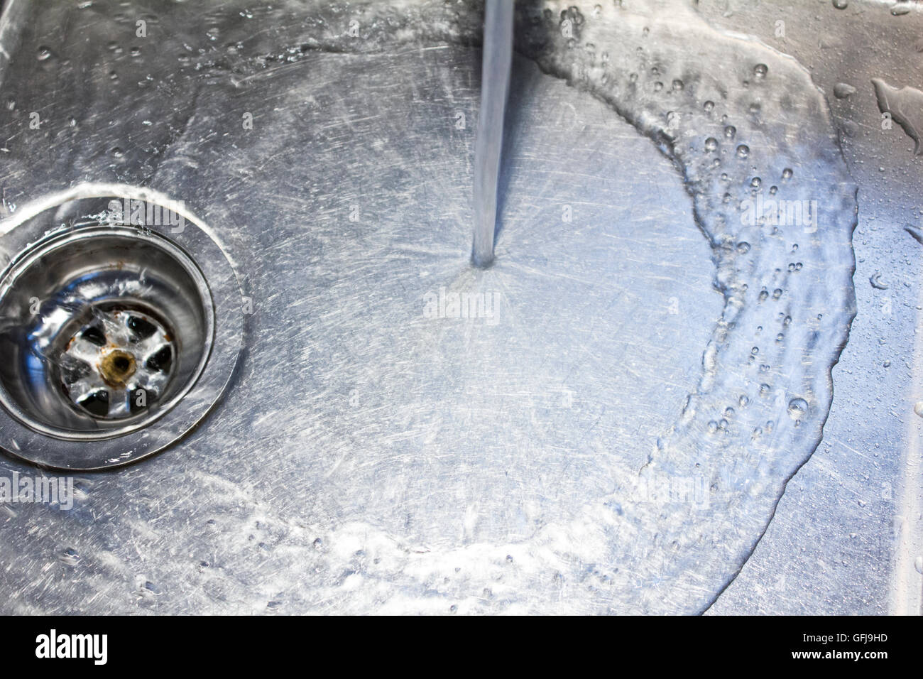 Water from a tap runs down the drain in a stainless steel sink Stock