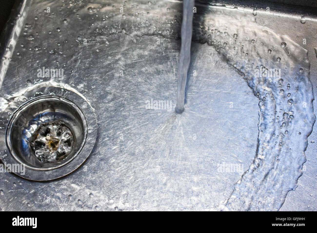 Water from a tap runs down the drain in a stainless steel sink Stock Photo