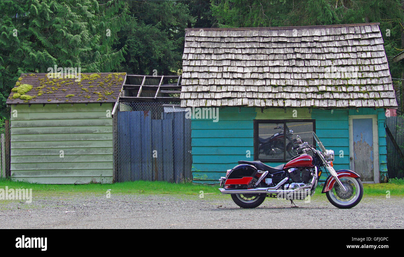 A motorcycle parked on the roadside in front of a colorful rustic cabin on Washington State's Highway 2. Stock Photo