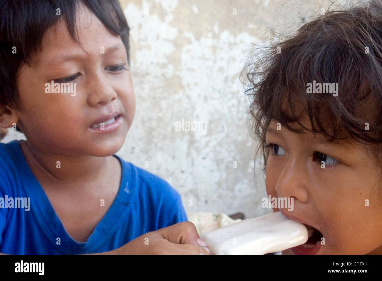 A boy is helping a young girl eat an ice cream bar in a slum in Kampong Cham, Cambodia. Stock Photo