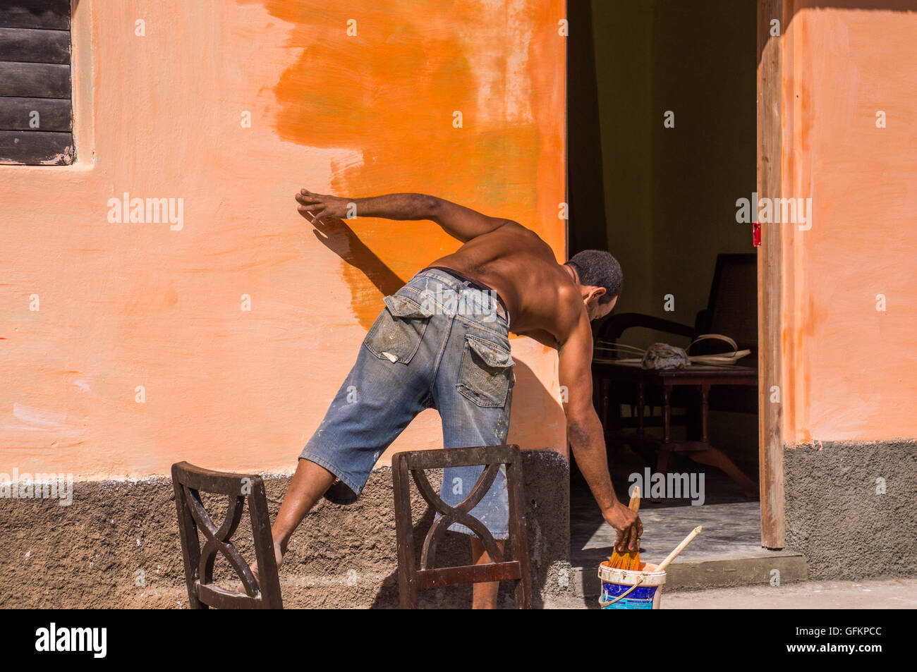 Trinidad, Cuba on December 30, 2015: A man is repainting a wall with a bright orange color. This illustrates the repainting of C Stock Photo