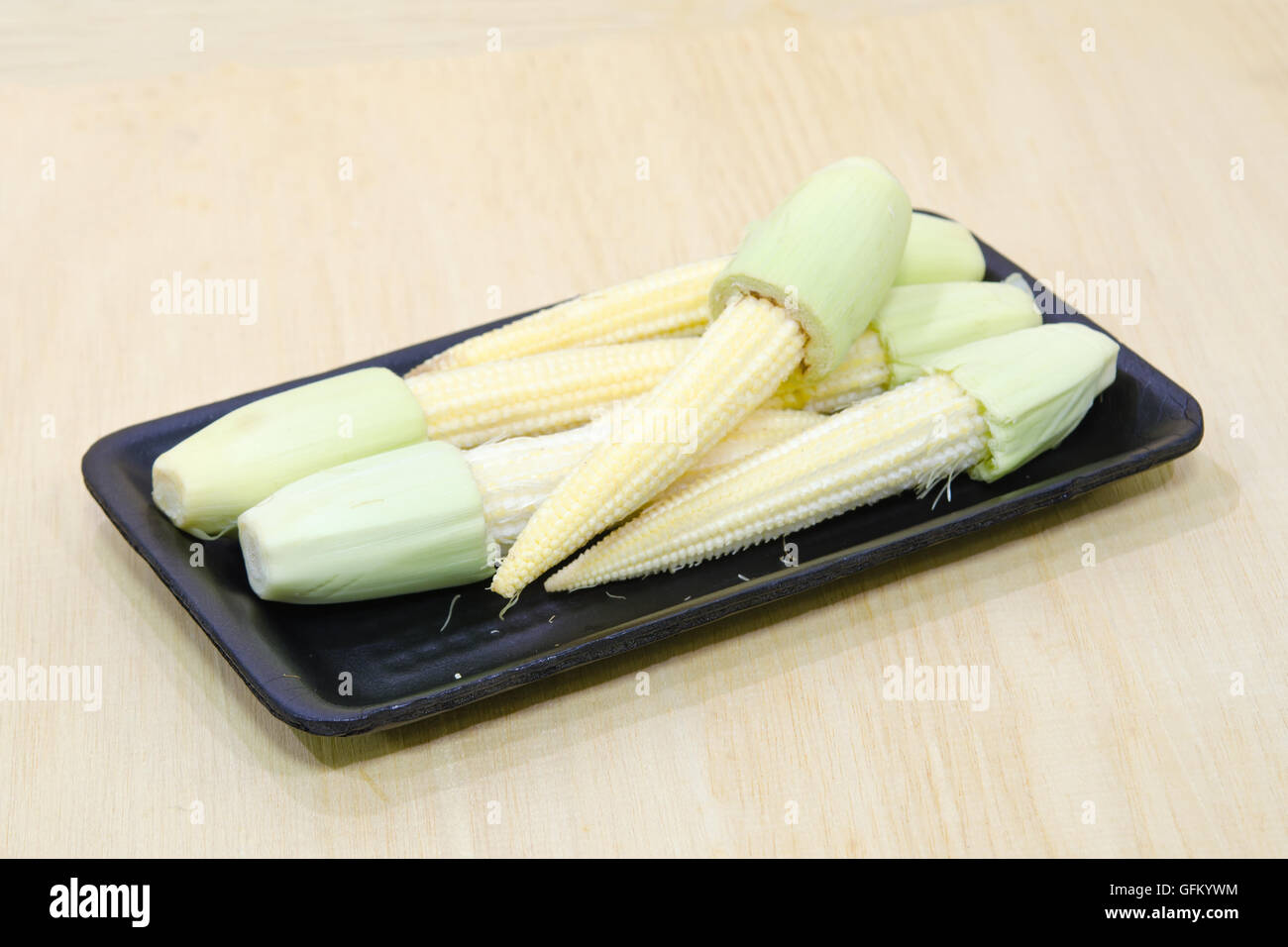 Baby corn fruit (also known as young corn, mini corn, cornlettes, candle corn, Zea mays L, Gramineae) grouped on black plate on Stock Photo
