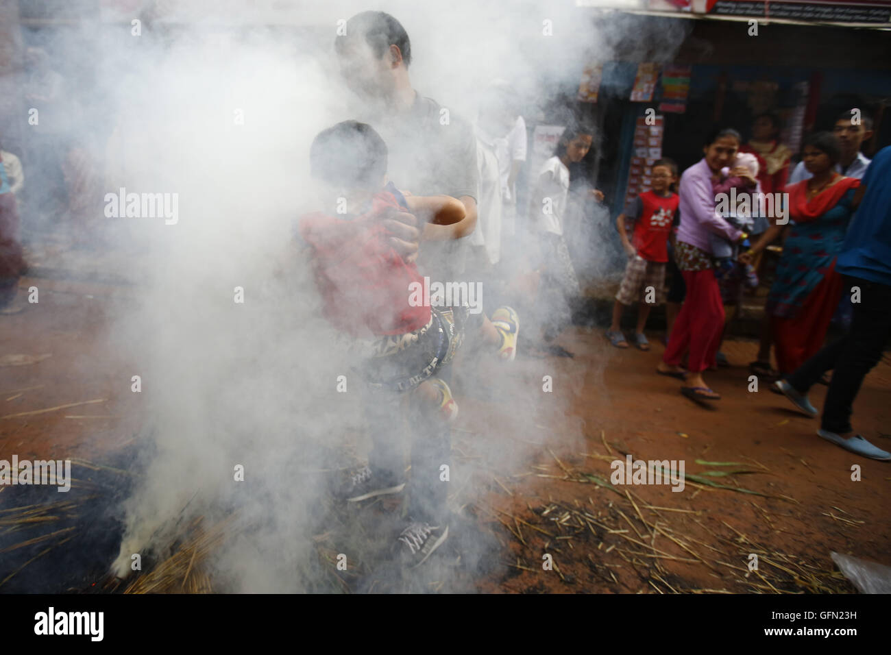 Bhaktapur, Nepal. 1st Aug, 2016. A Nepalese man draws his child towards fire of burnt straw effigy of mythical demon Ghanta Karna as celebrations for his death during the Hindu festival of Gathe Mangal in Dattatreya Square, Bhaktapur, Nepal on Monday, August 1, 16. It is believed according to myths that by burning the demon rid evil spirits. © Skanda Gautam/ZUMA Wire/Alamy Live News Stock Photo