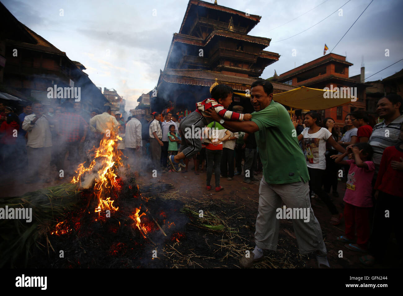 Bhaktapur, Nepal. 1st Aug, 2016. A Nepalese man draws his child towards fire of burnt straw effigy of mythical demon Ghanta Karna as celebrations for his death during the Hindu festival of Gathe Mangal in Dattatreya Square, Bhaktapur, Nepal on Monday, August 1, 16. It is believed according to myths that by burning the demon rid evil spirits. © Skanda Gautam/ZUMA Wire/Alamy Live News Stock Photo