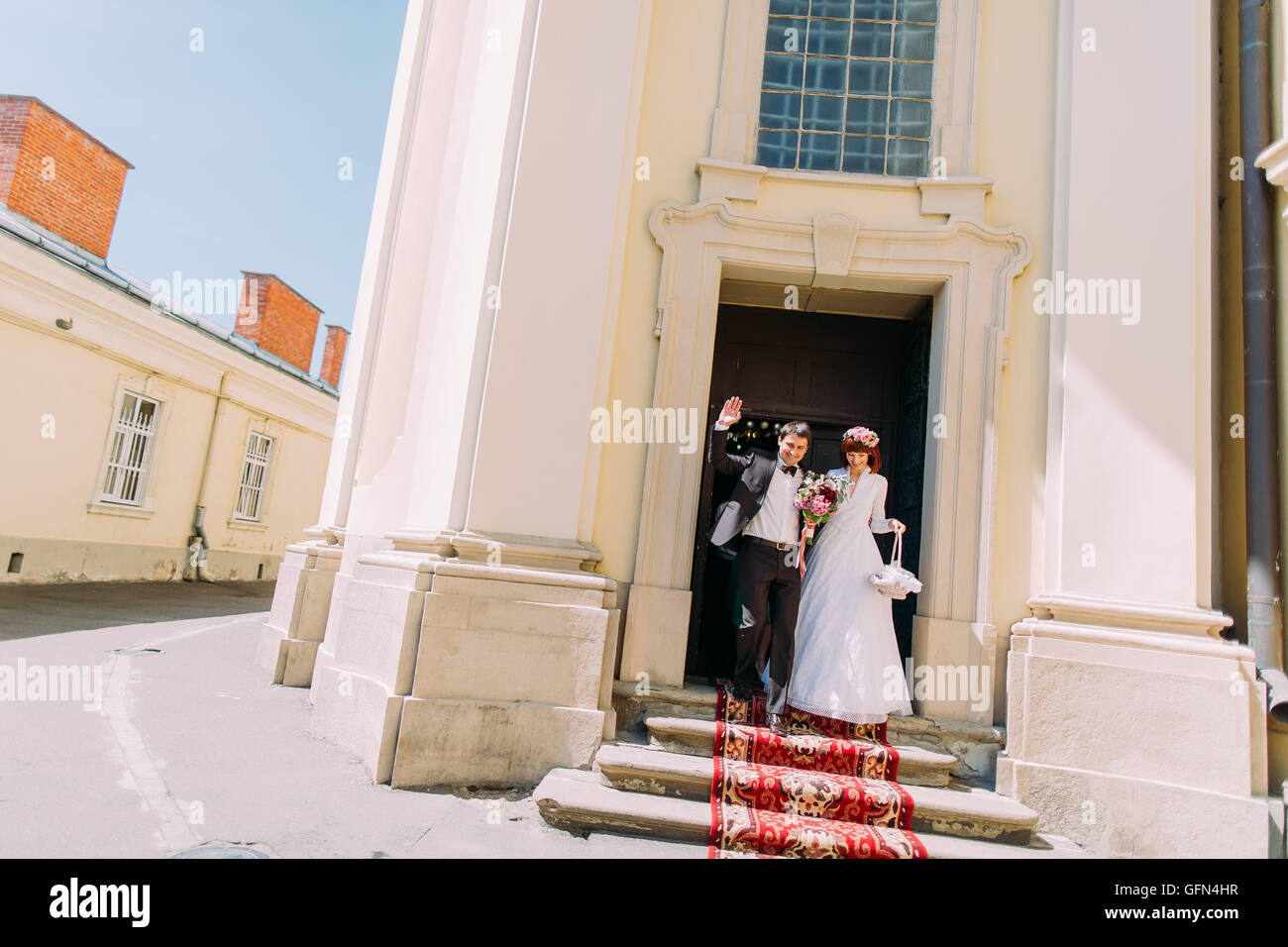 Stylish gorgeous bride and elegant groom walking out of church, happy newlyweds Stock Photo