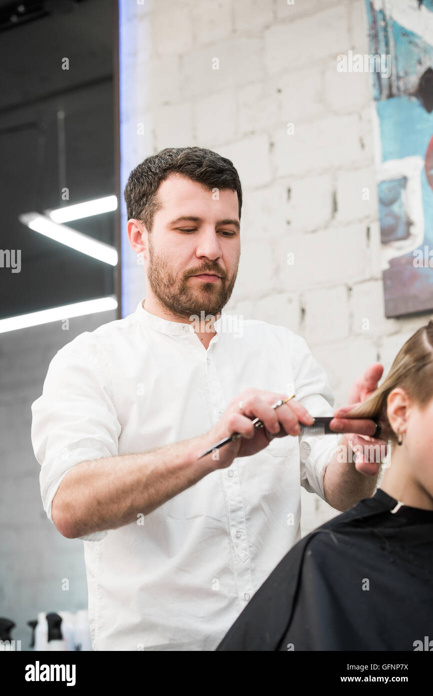 Male hairdresser making haircut for a client in professional