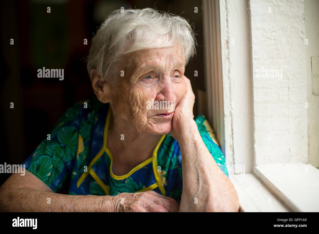 An elderly lady skeptically looking out the window. Stock Photo