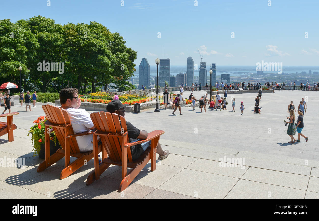 Mount Royal Park viewpoint, Montreal, Canada - two young men sitting in wooden chairs people watching and looking at view of Mon Stock Photo