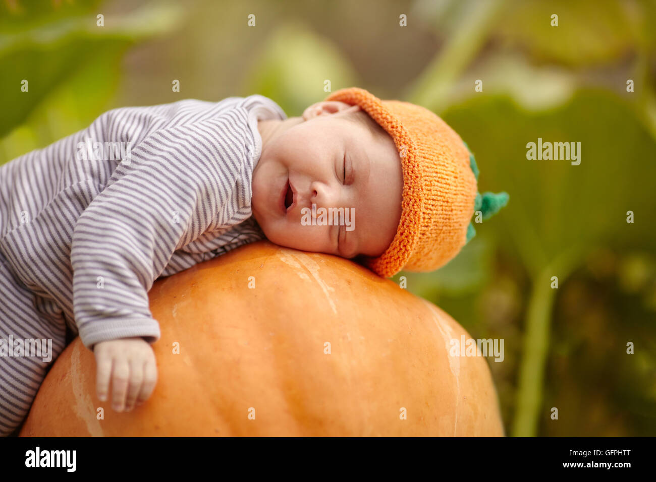 baby with pumpkin hat sleeping on big orange pumpkin Stock Photo