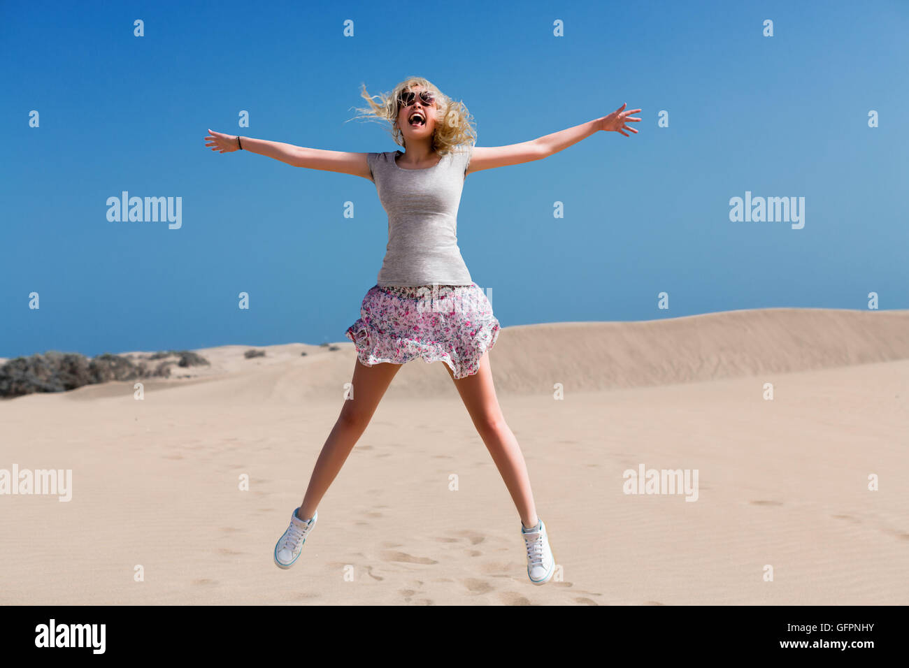 A young girl wearing a skirt jumping on the sand desert Stock Photo