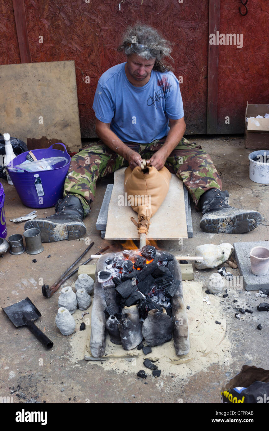 Artist using a hand pumped bellows to smelt metal in a simple kiln for moulding at Flameworks, Plymouth, UK Stock Photo